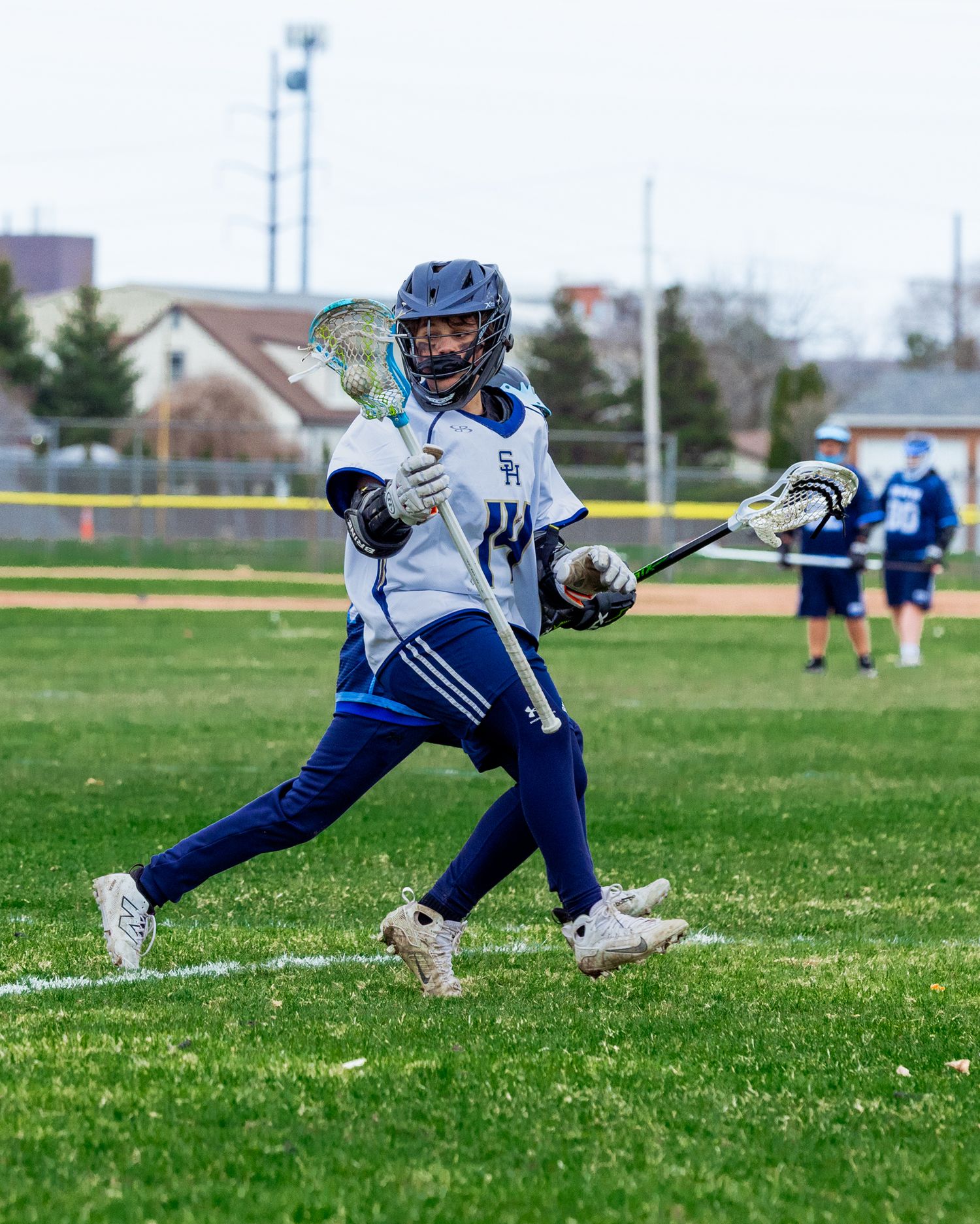 Lacrosse player in blue uniform makes dynamic move with stick during game.