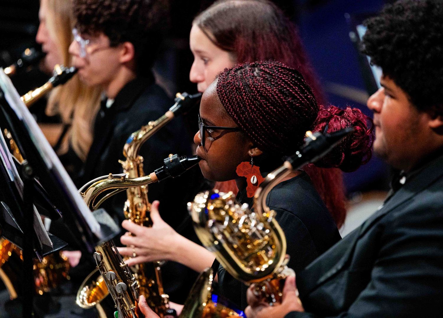 Musicians play brass and woodwind instruments in an orchestra performance with dark lighting.