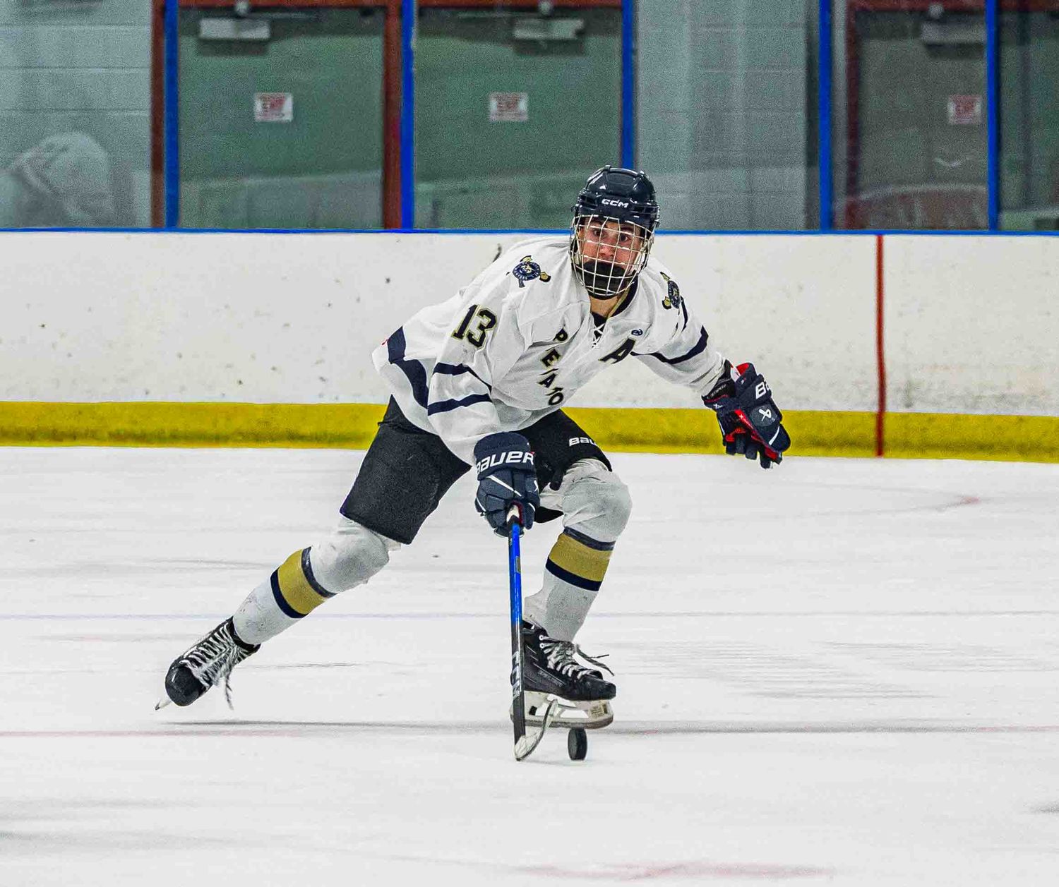 Hockey player #13 in white and navy uniform skating on indoor ice rink during a game.