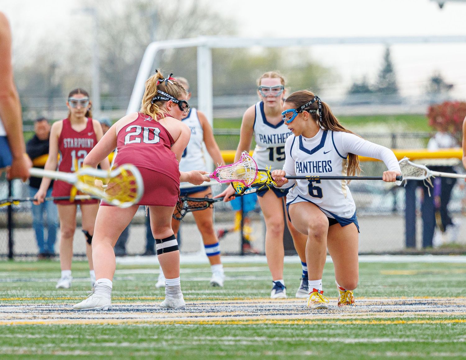 Female lacrosse players compete on field, Panthers player number 6 defending against opponent number 20 during game.