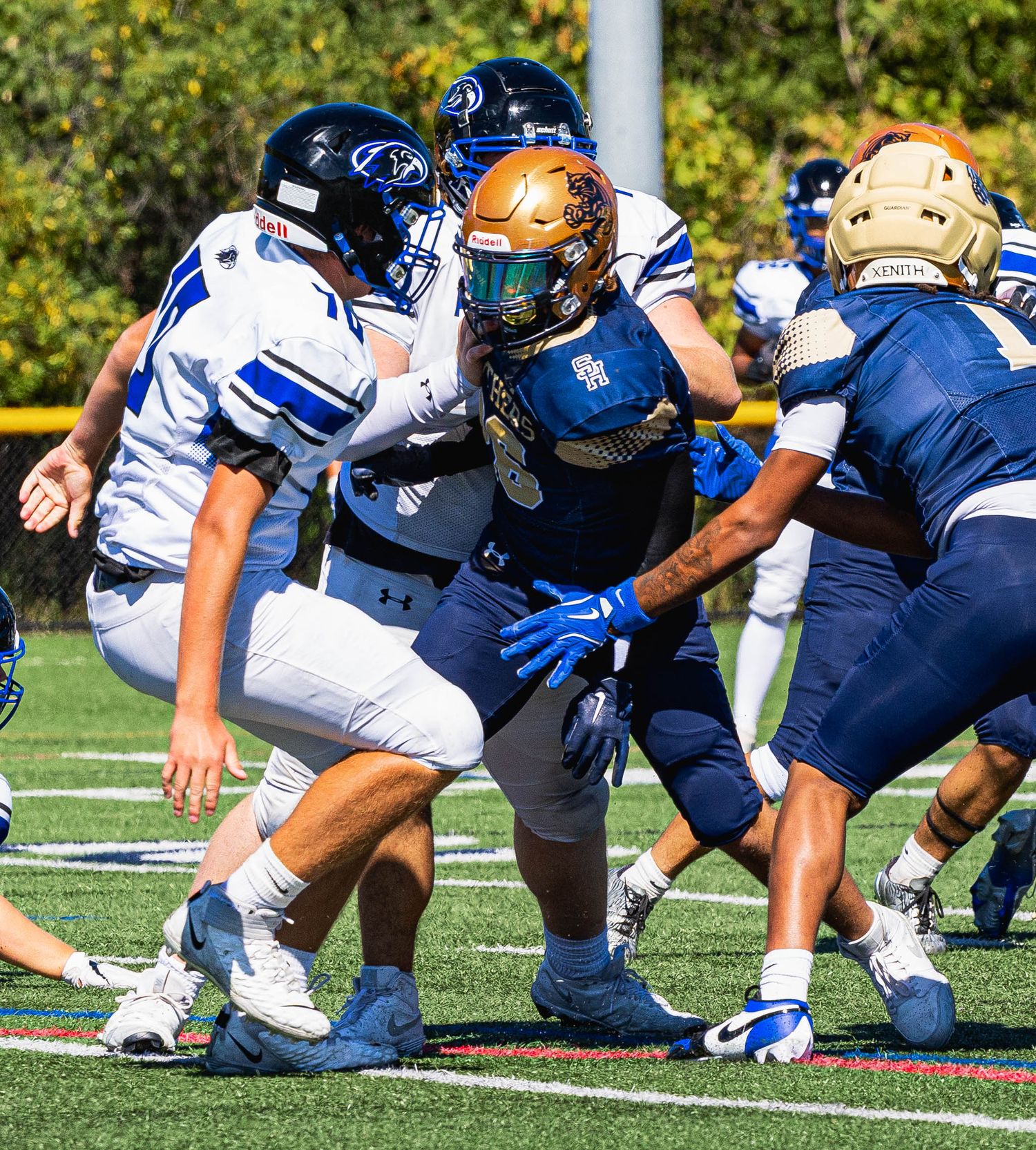 College football players in navy and white uniforms clash on a sunny field during an intense line of scrimmage play.