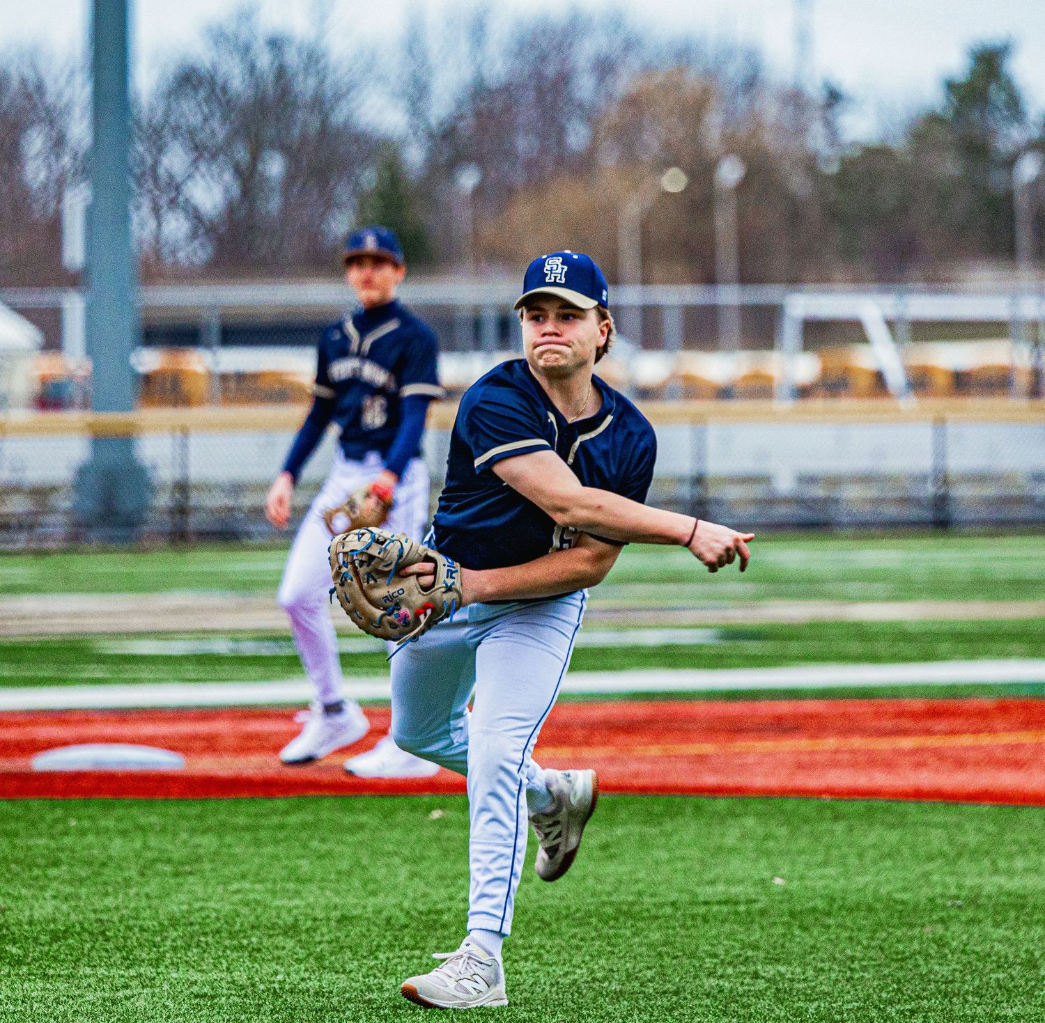 Baseball pitcher in navy uniform winding up to throw on turf field during game.