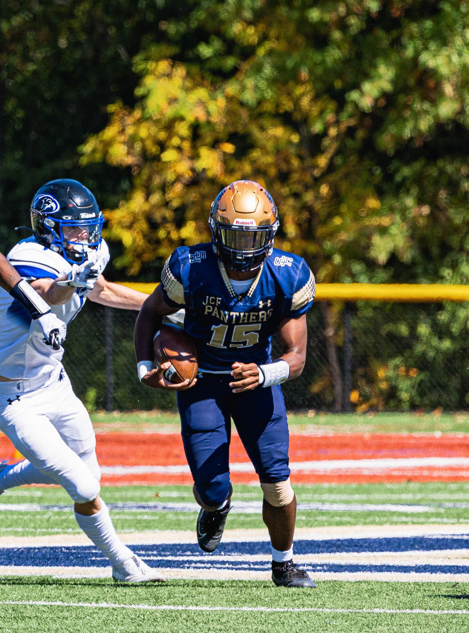 Football player number 15 in blue and gold uniform running with ball during outdoor game.
