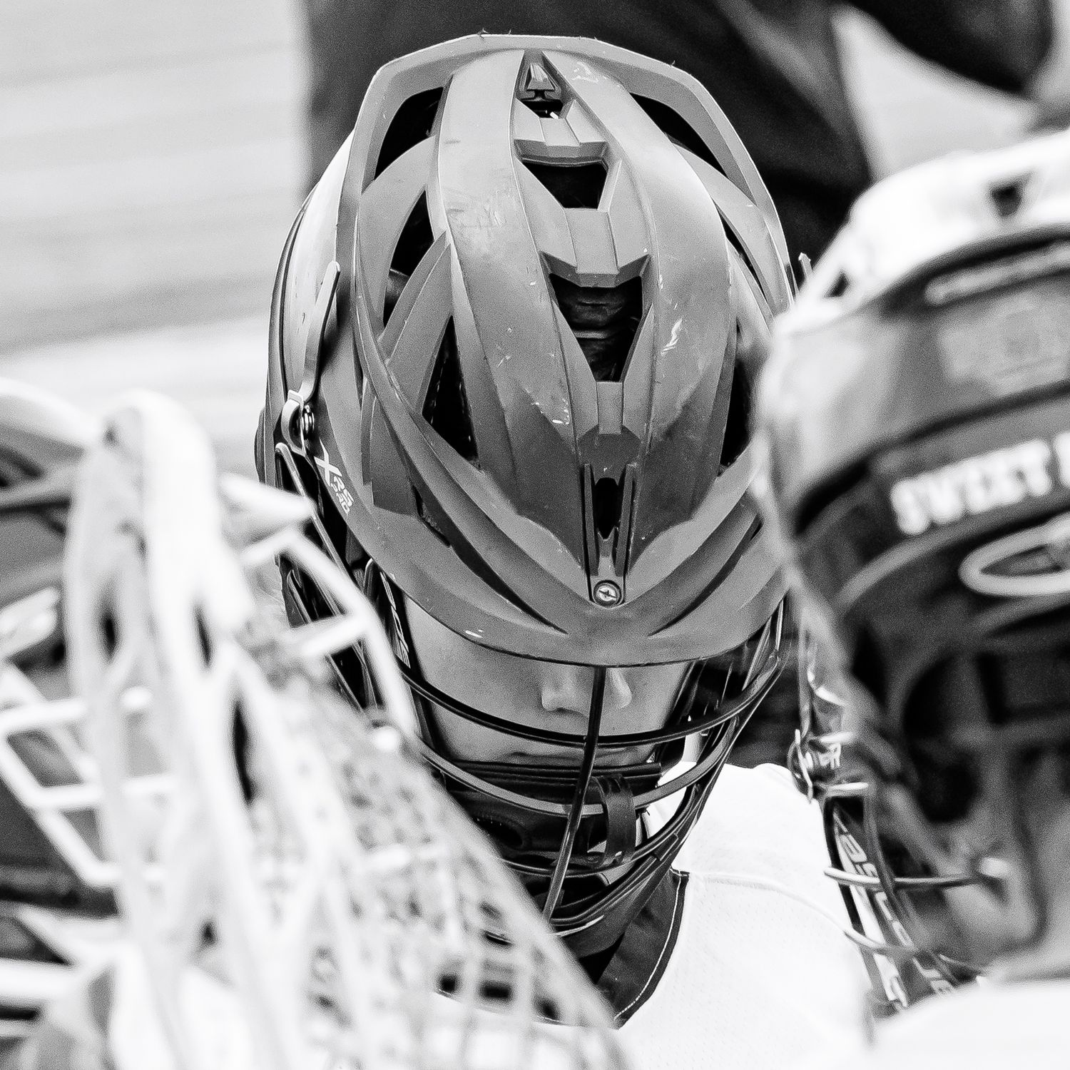 Black and white photo of lacrosse players wearing helmets with face guards during a game.