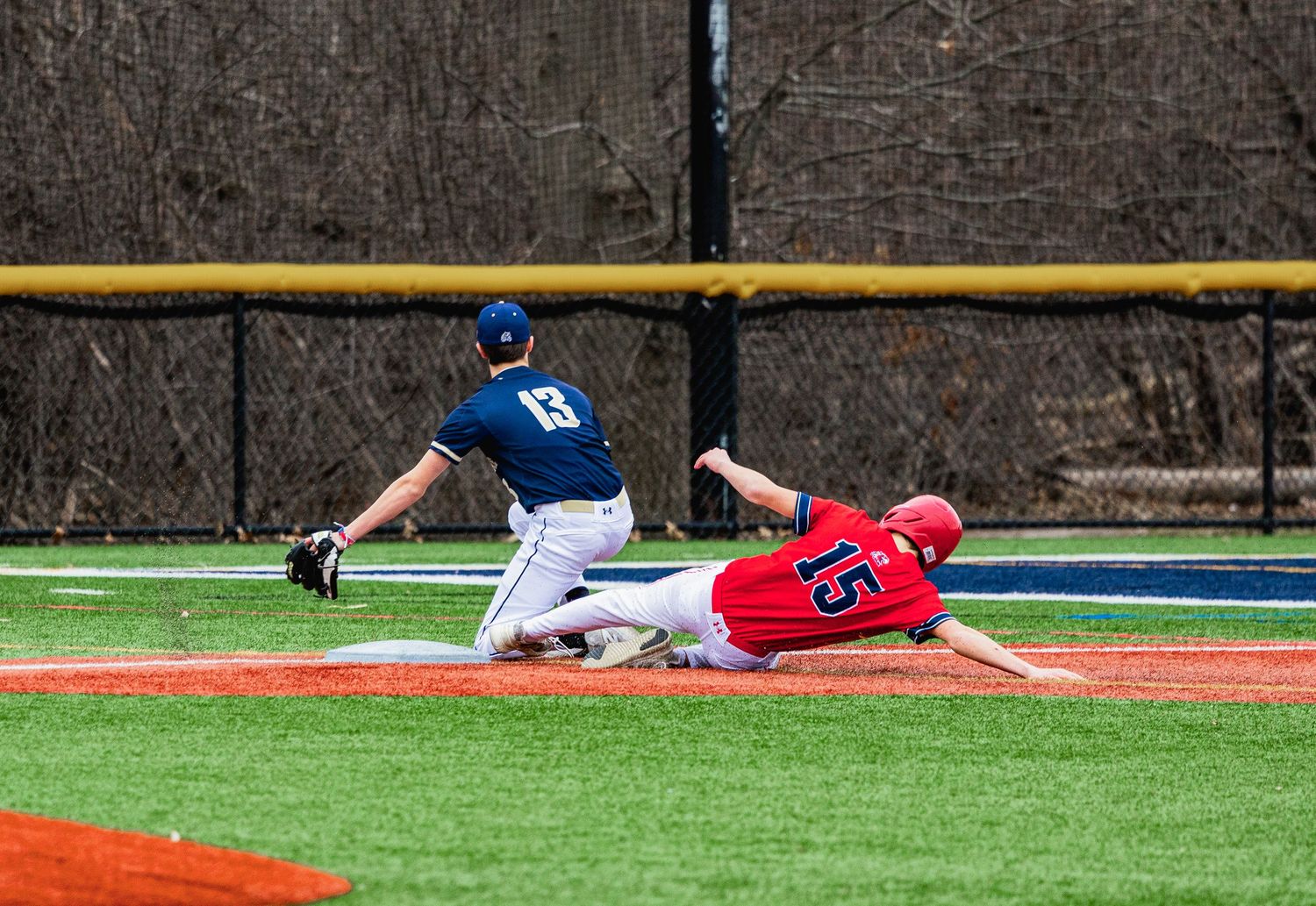 A baseball player in red slides into base as a navy-uniformed fielder attempts a tag during a game.