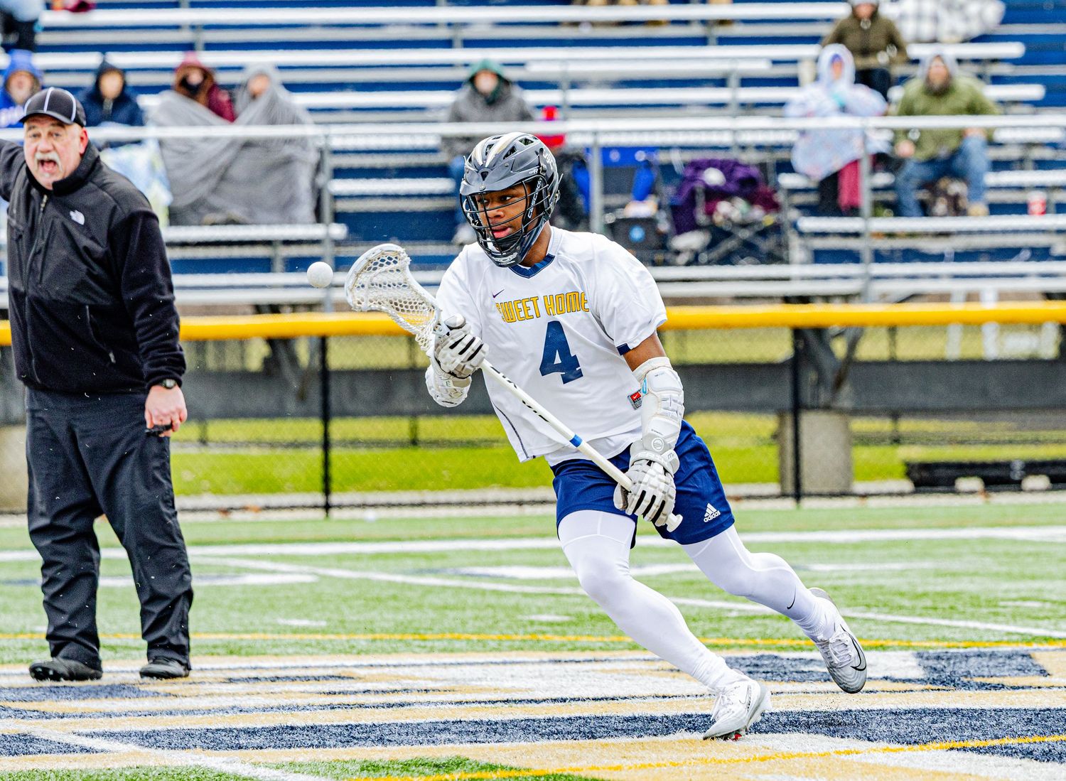 Lacrosse player #4 in blue and white uniform running with stick during an outdoor game.