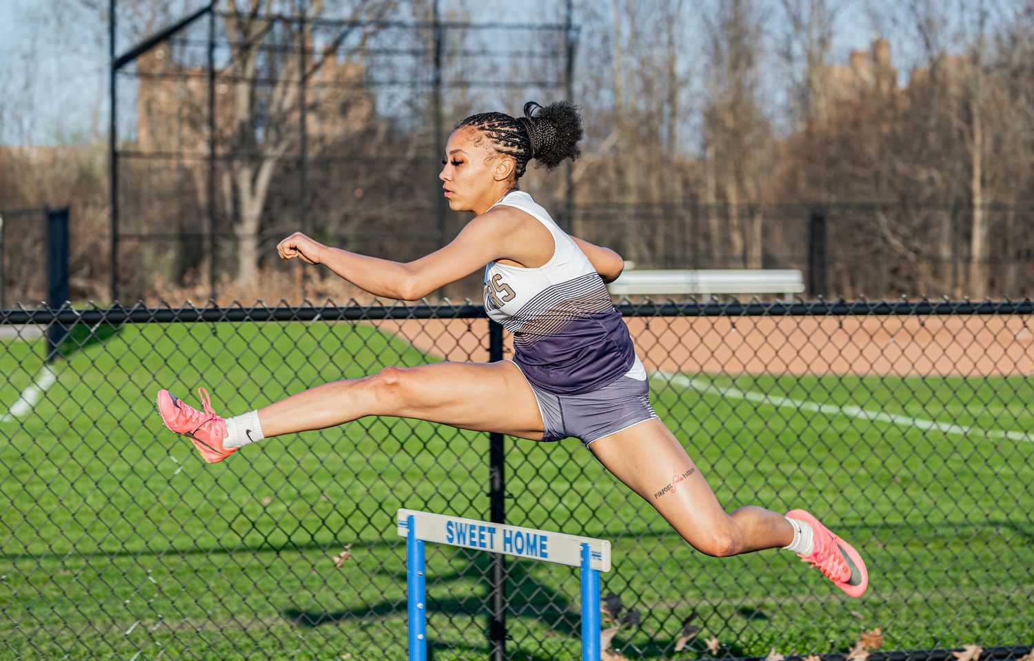 Female track athlete leaping over a hurdle during outdoor practice at Sweet Home track facility.
