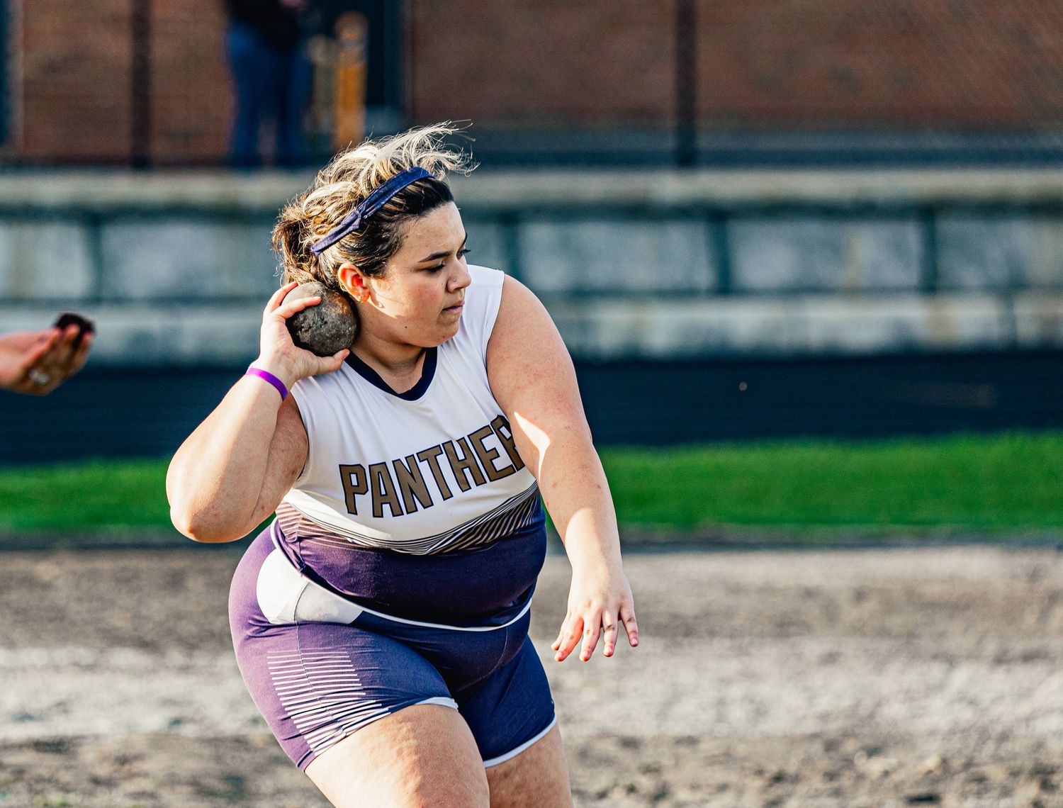 A female Panthers athlete prepares to throw a shot put during an outdoor track and field competition.