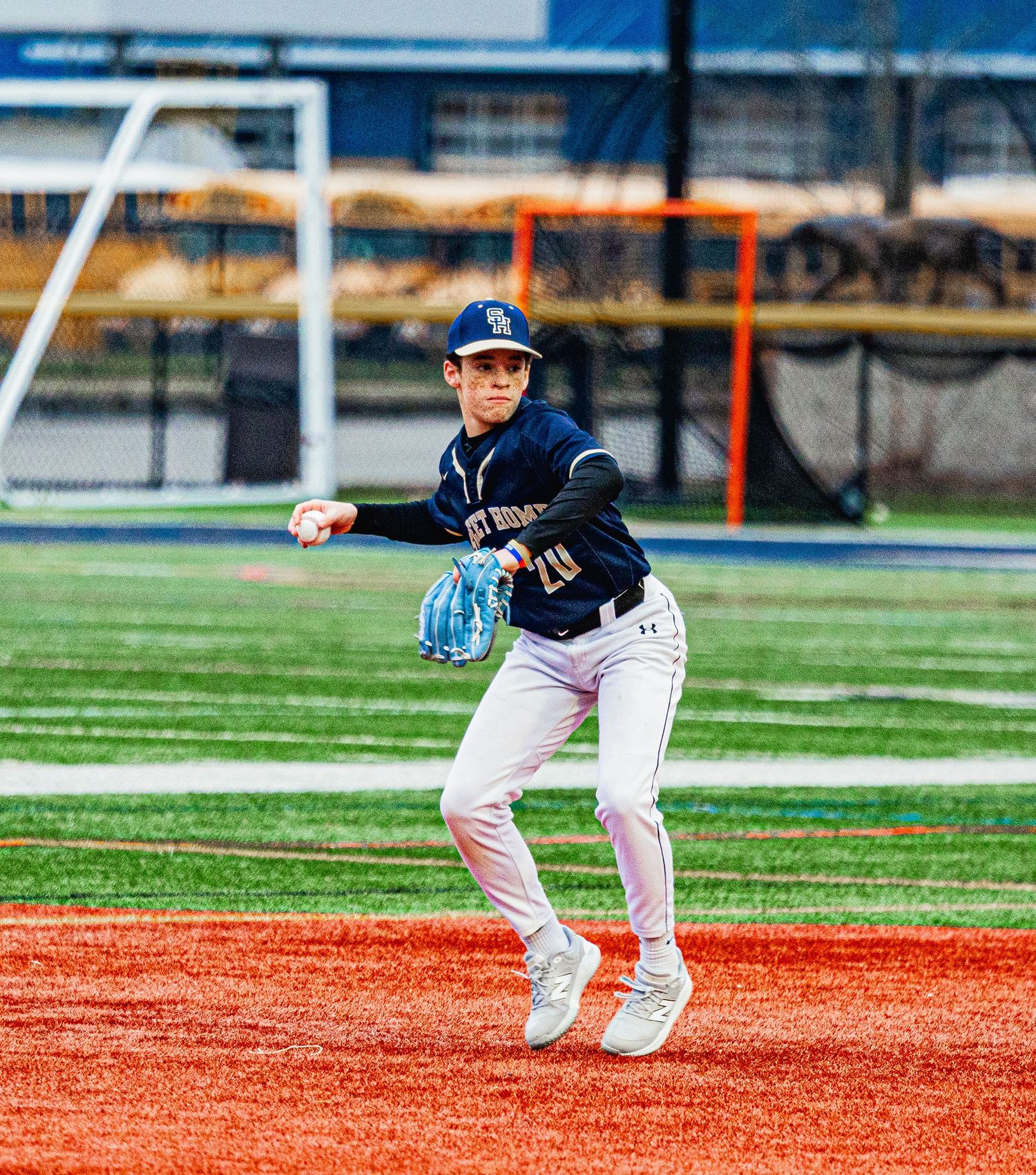 Youth baseball infielder in navy uniform fields ball on colorful artificial turf diamond.