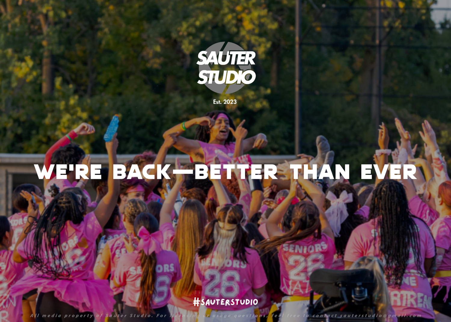 Crowd of dancers in pink outfits performing at an outdoor festival with colorful lighting and 'We're Back' text overlay.