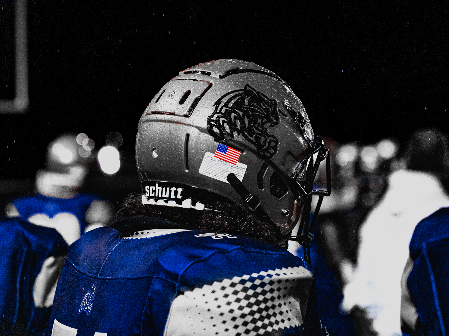 A row of football players in blue and black uniforms stand on the sidelines during a game.