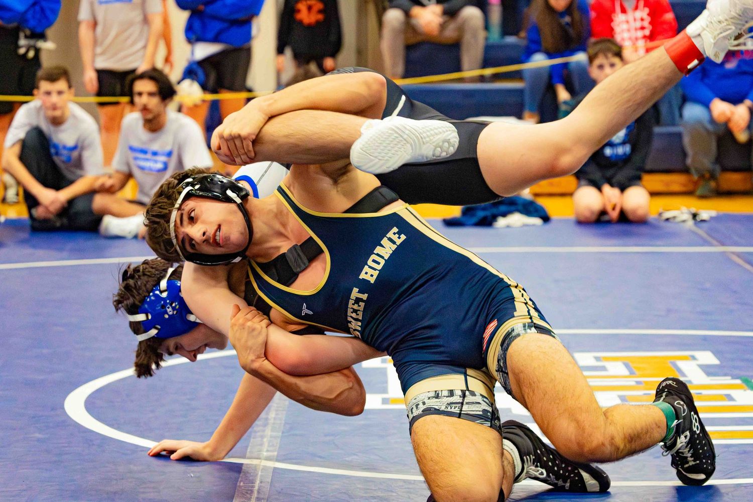 Two wrestlers competing in a high school wrestling match on a blue mat during a tournament.