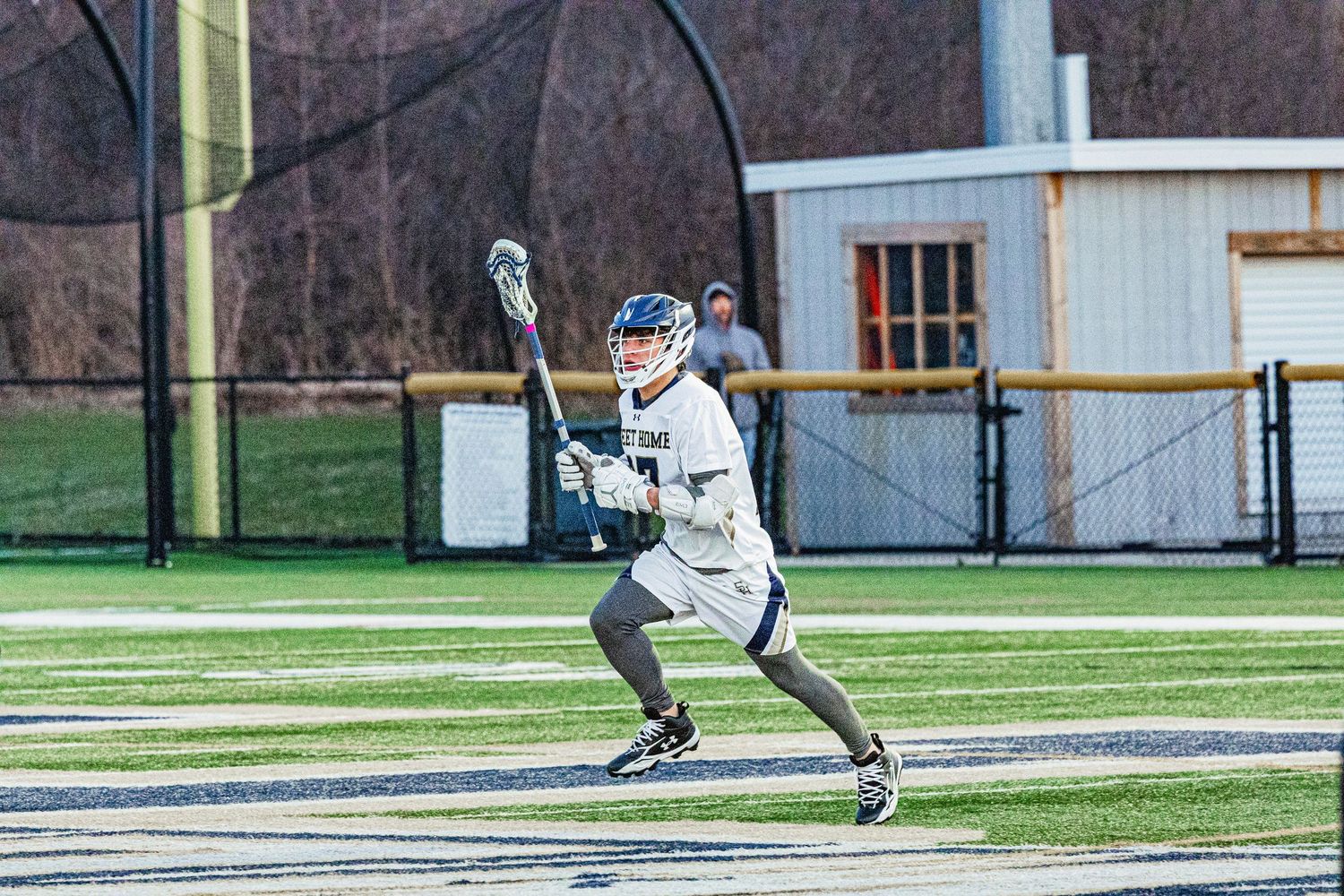 Lacrosse player in white uniform cradling ball with stick on green turf field during outdoor game.