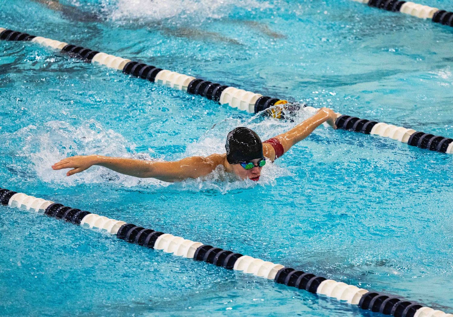A swimmer performs the butterfly stroke in a pool with lane dividers during a competitive swim meet.