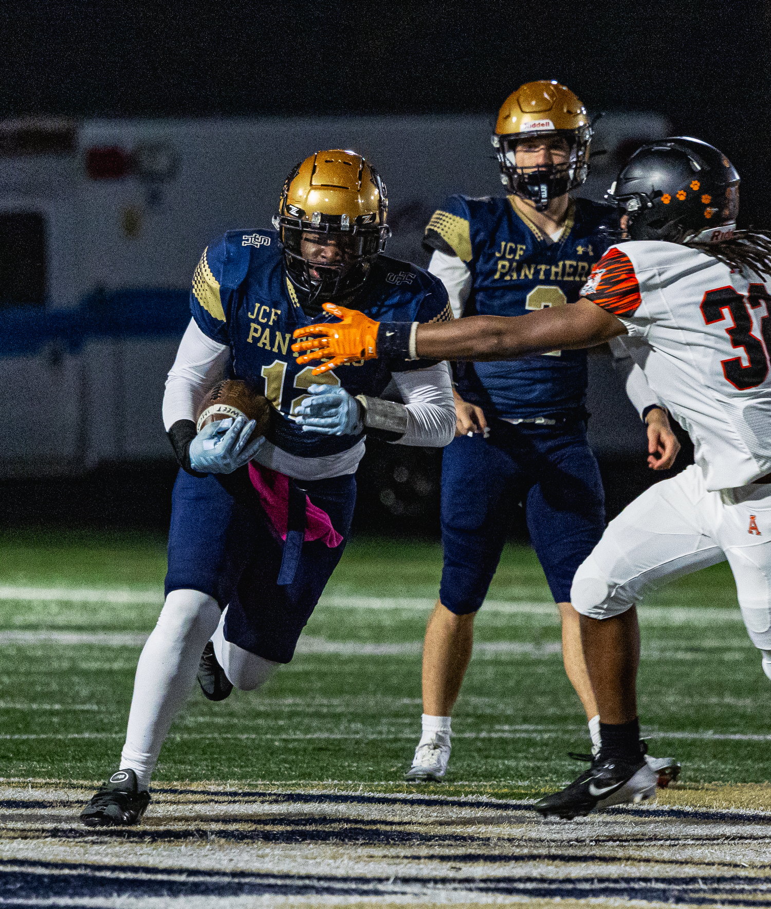Jefferson Panthers football player runs with the ball during a night game against an opponent in orange jerseys.