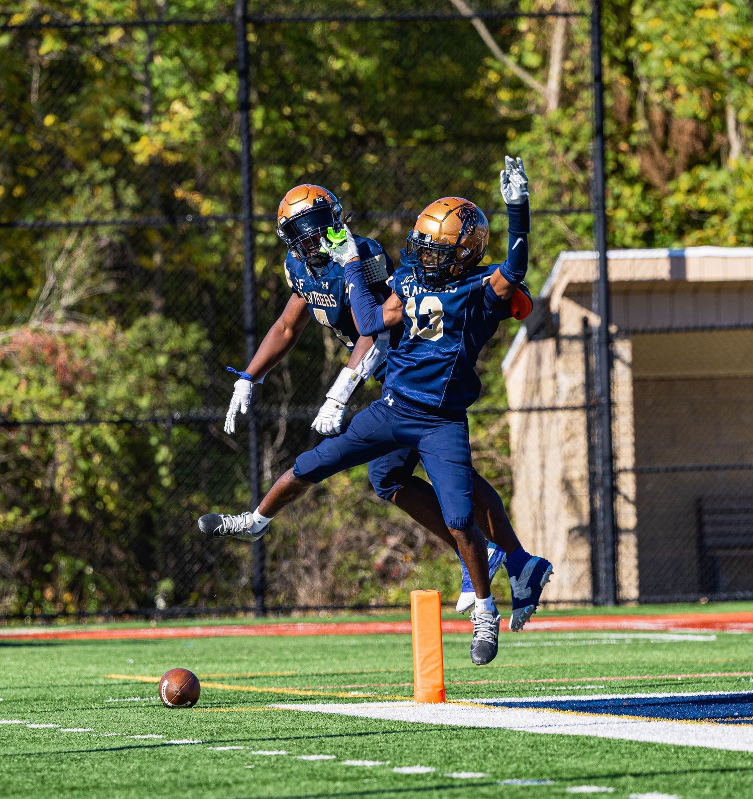 Football players celebrating touchdown in navy and gold uniforms on turf field.