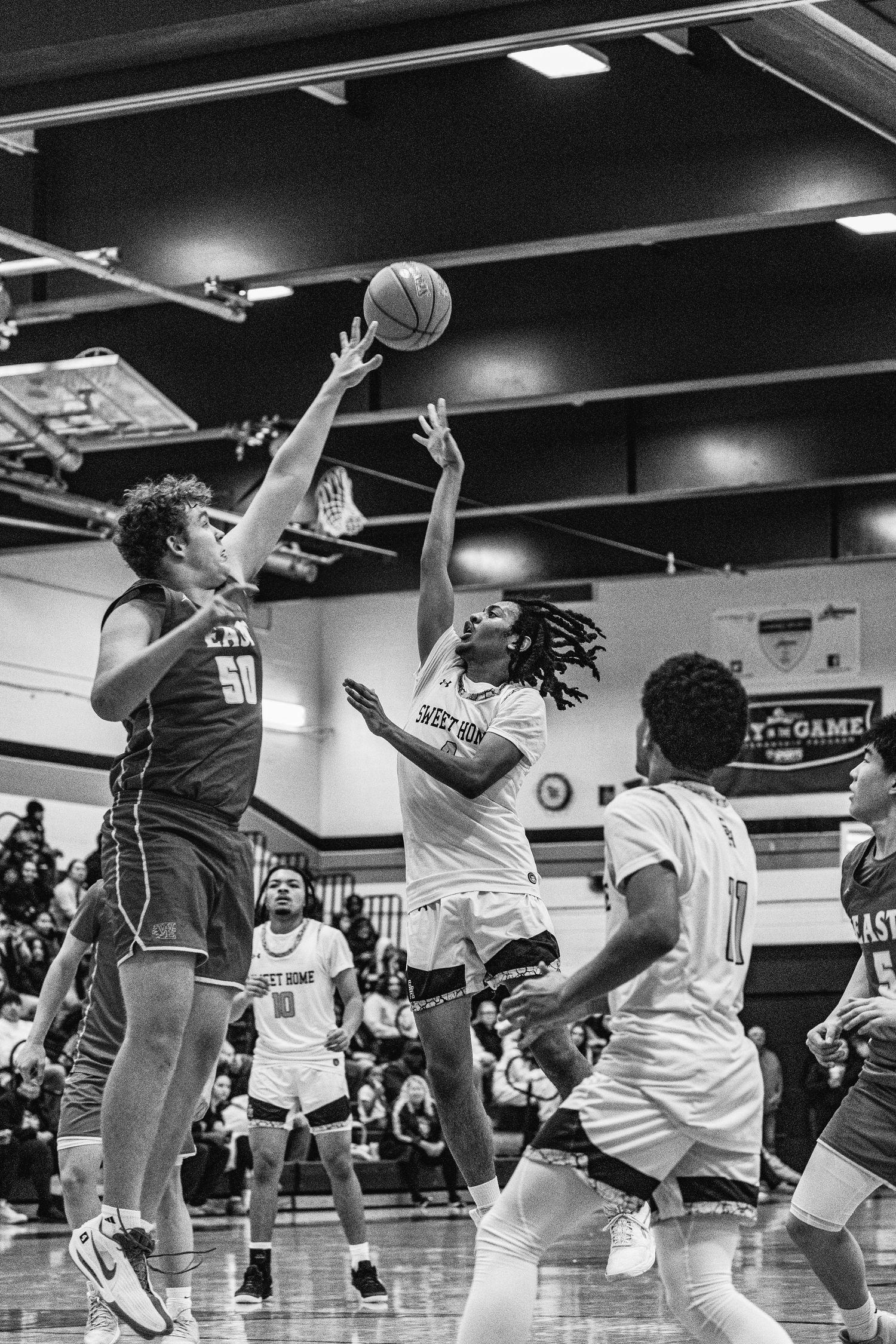 A basketball player attempts a shot over a defender numbered 50 during an indoor high school game.