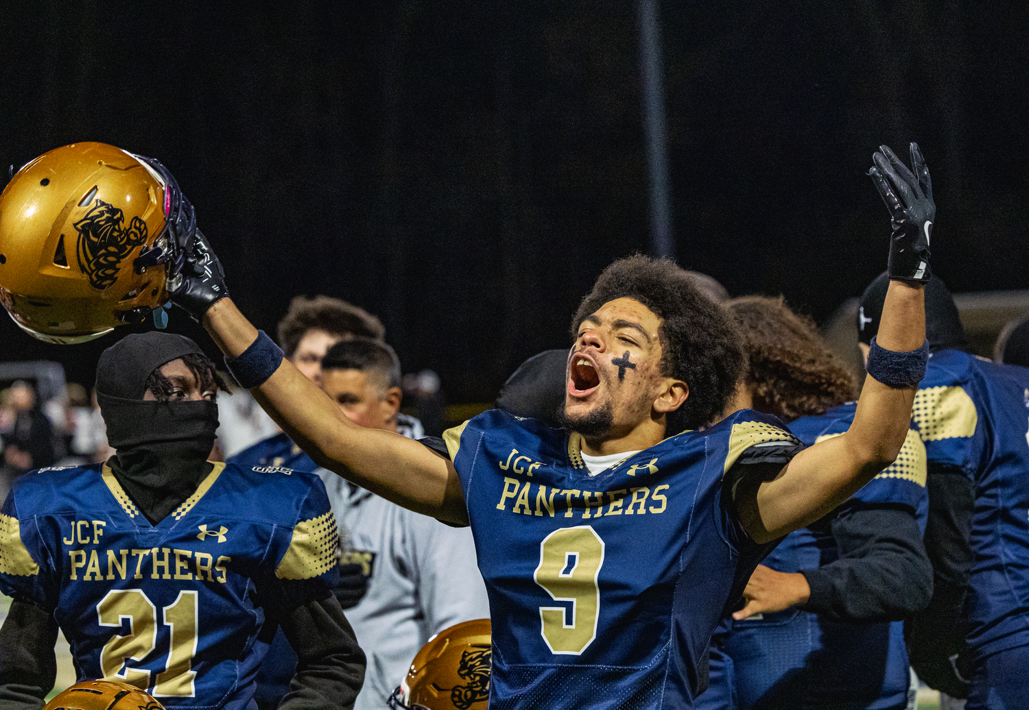 High school Panthers football player number 9 celebrates victory, raising helmet and cheering with teammates.