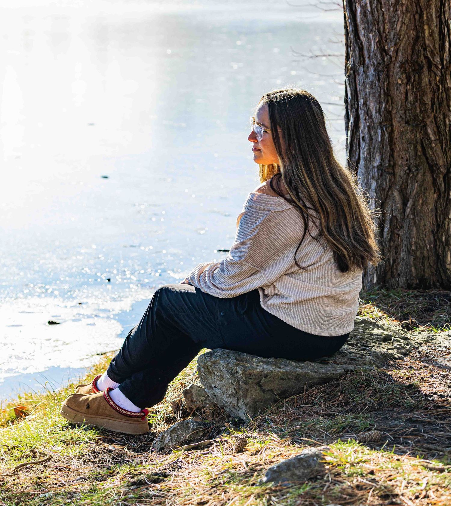 Person in beige sweater sits against tree trunk in outdoor setting during daytime.
