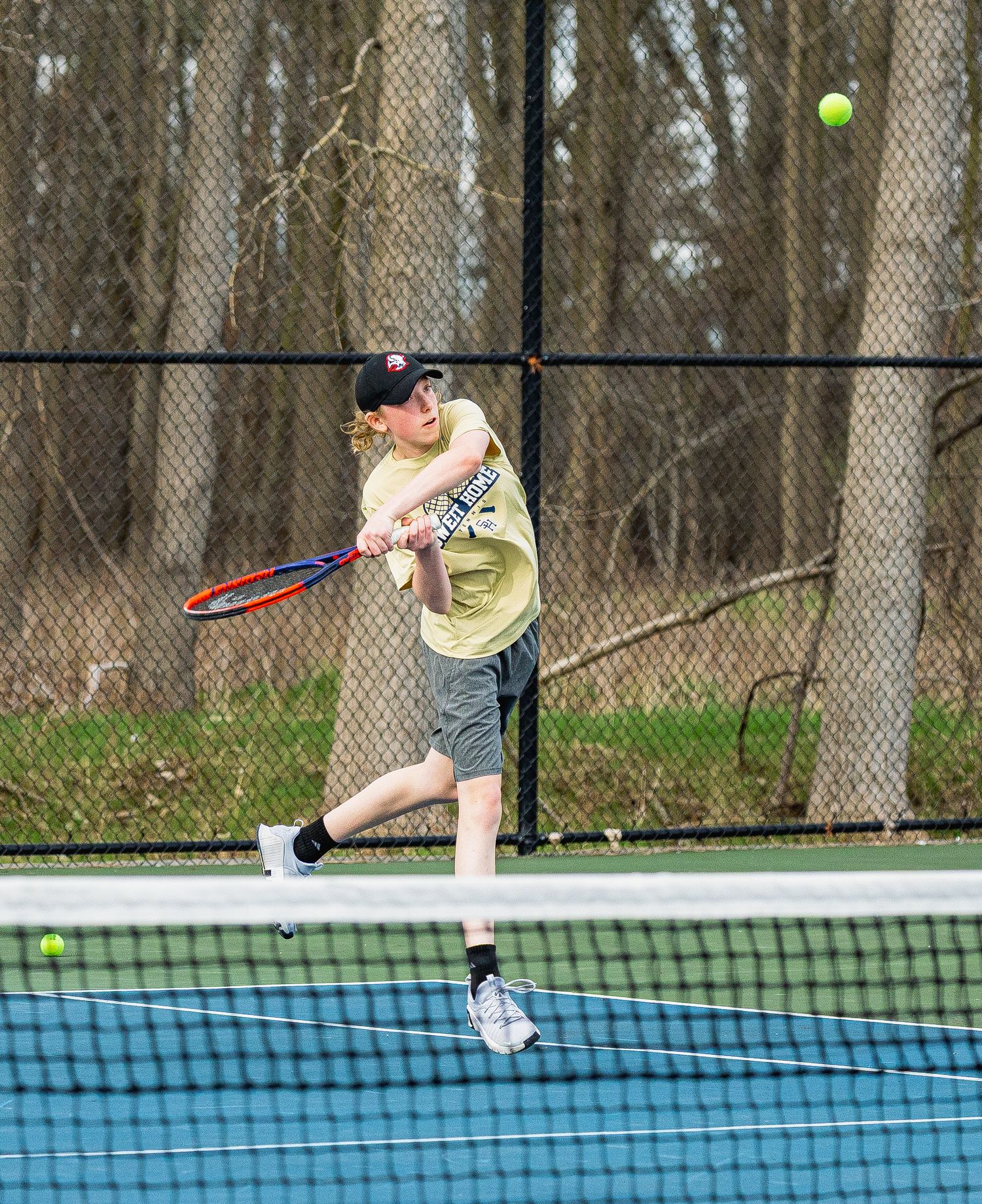 Young tennis player hitting a backhand shot on an outdoor court during a spring match.