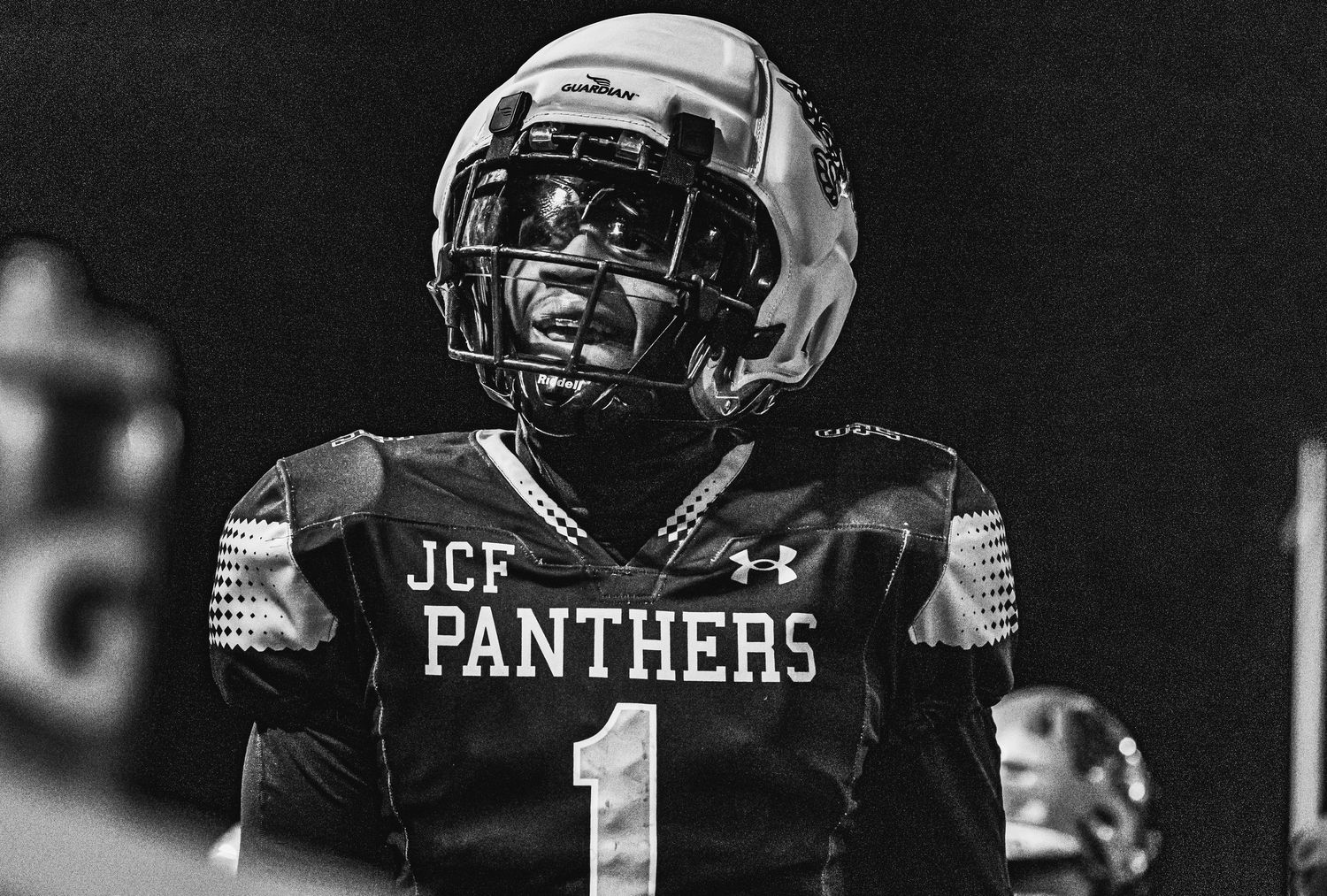 JCF Panthers football player #1 in black uniform and helmet stands on field in dramatic black and white photo.