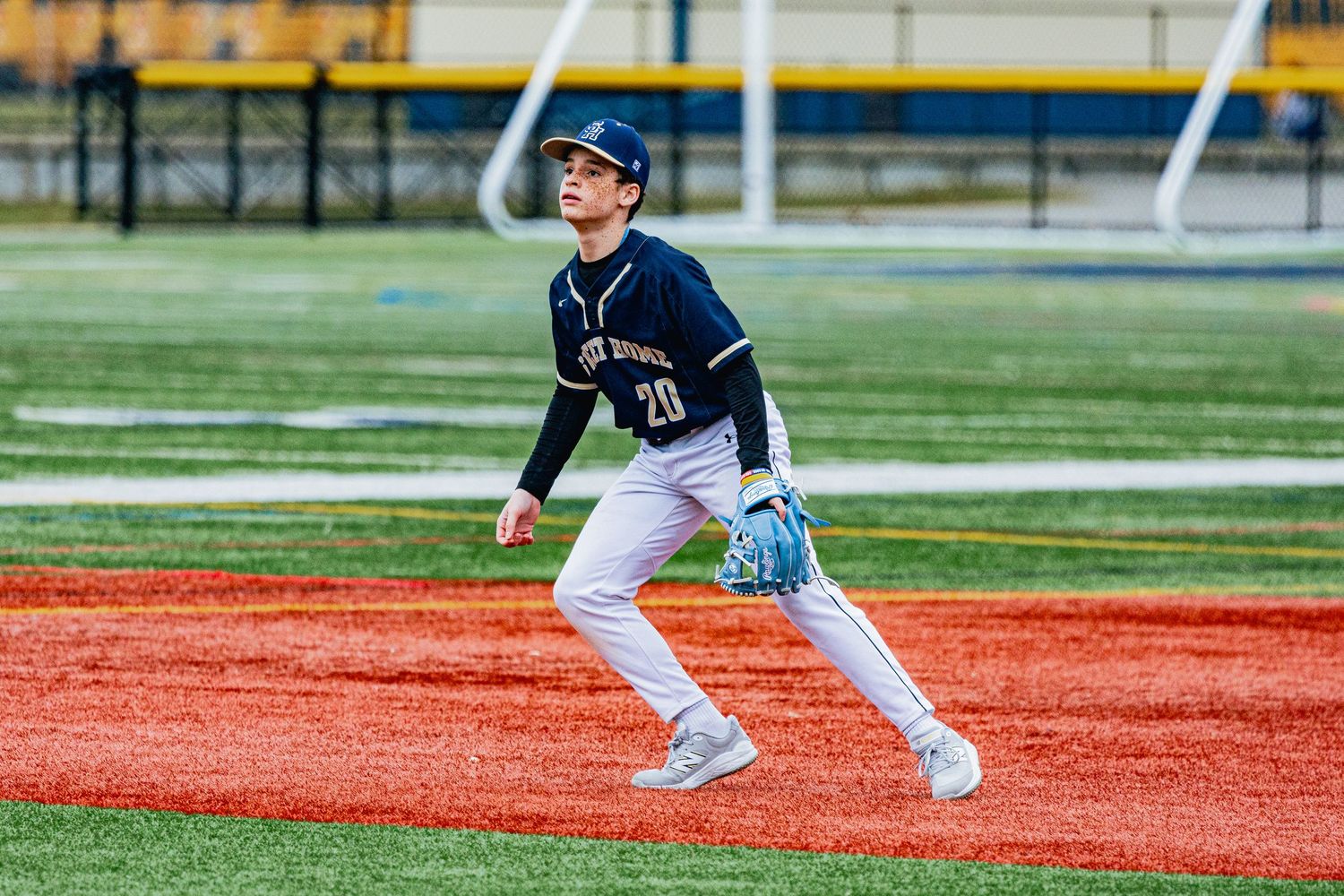 Baseball infielder in navy uniform ready for play on red and green artificial turf field.
