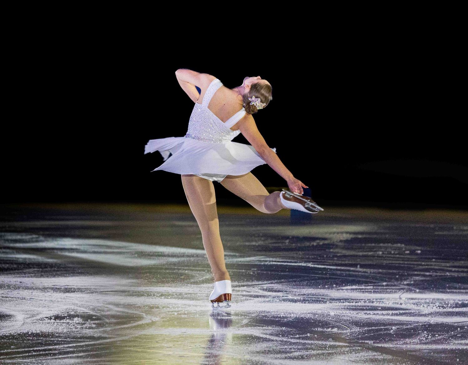 Figure skater in white dress performs graceful spin on ice during competitive performance.