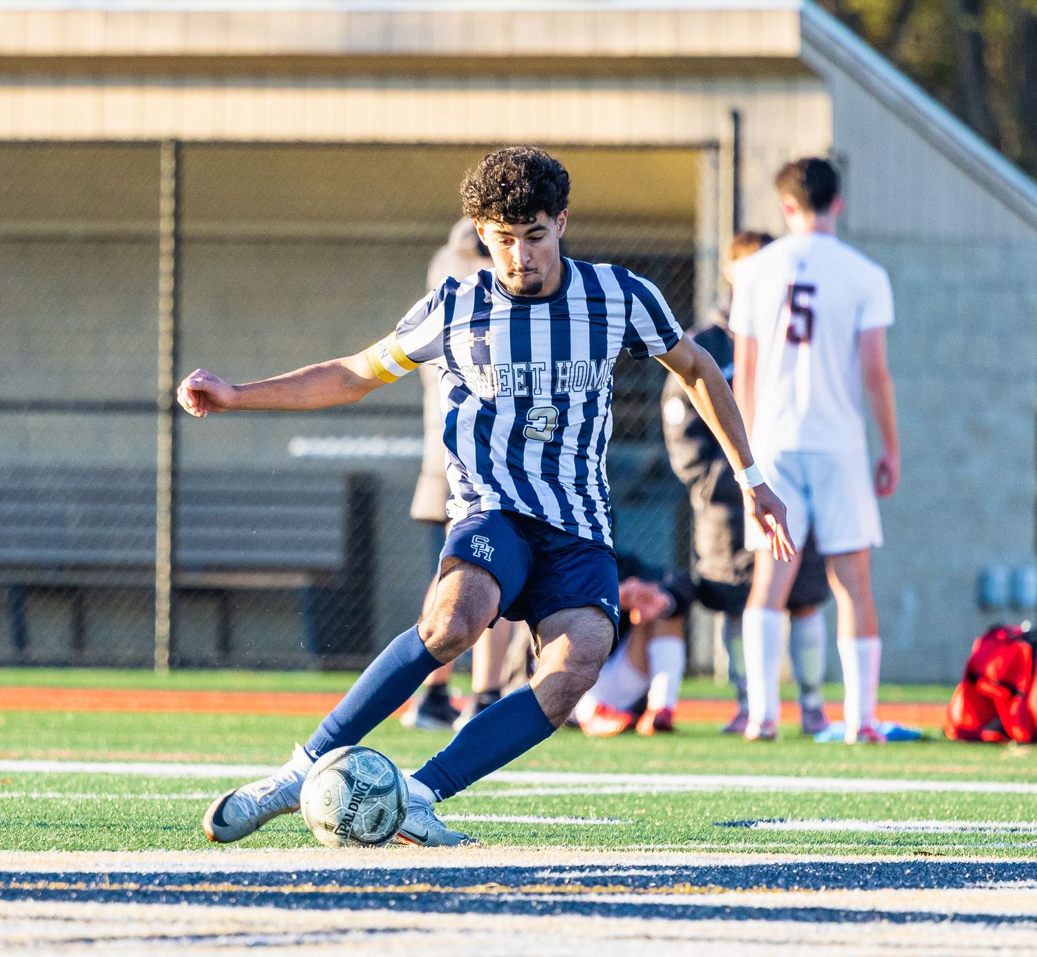 Soccer player in striped jersey slides to make a tackle during competitive match on artificial turf field.