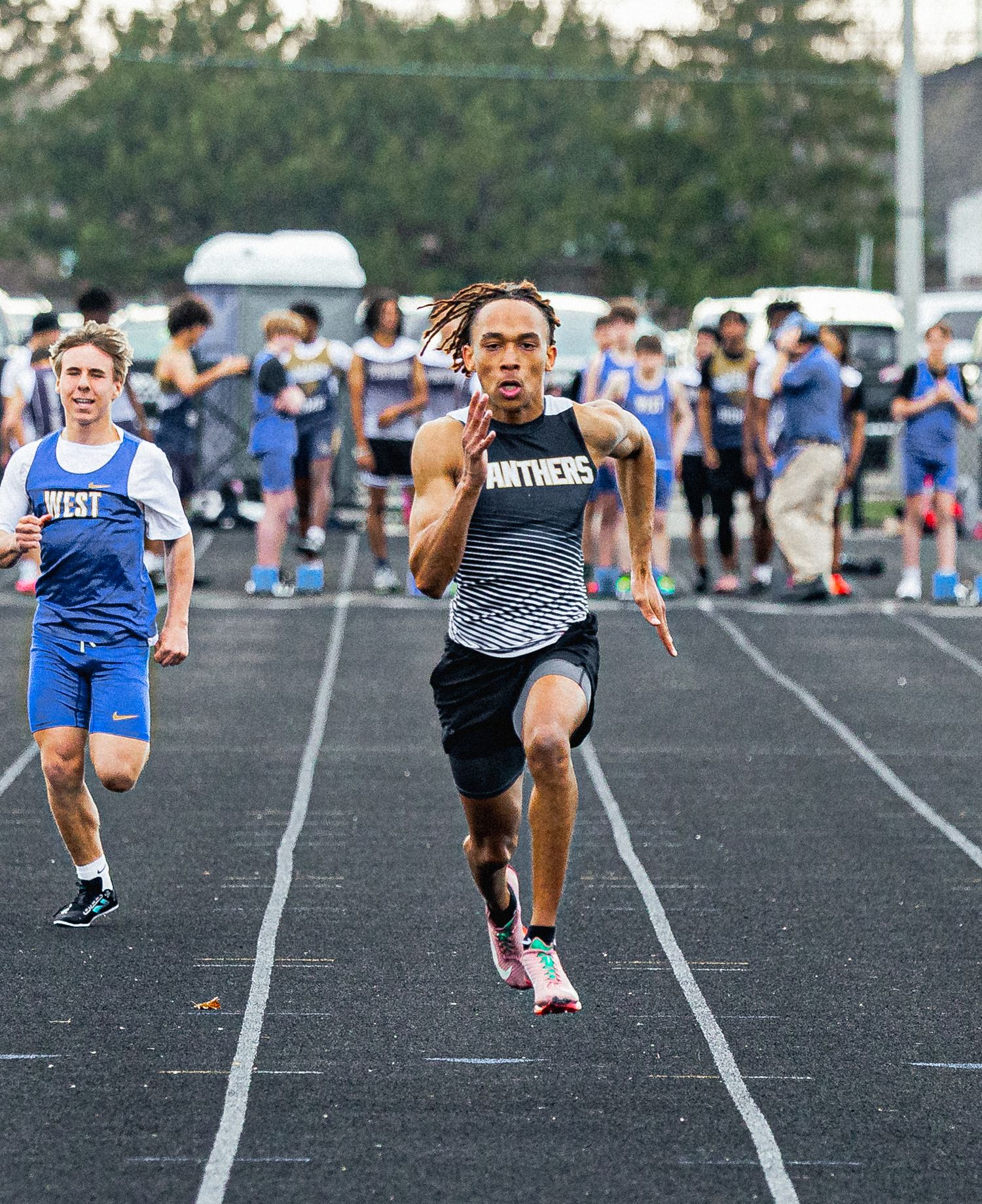 Panthers sprinter leads West competitor in high school track race on black asphalt track during outdoor meet.