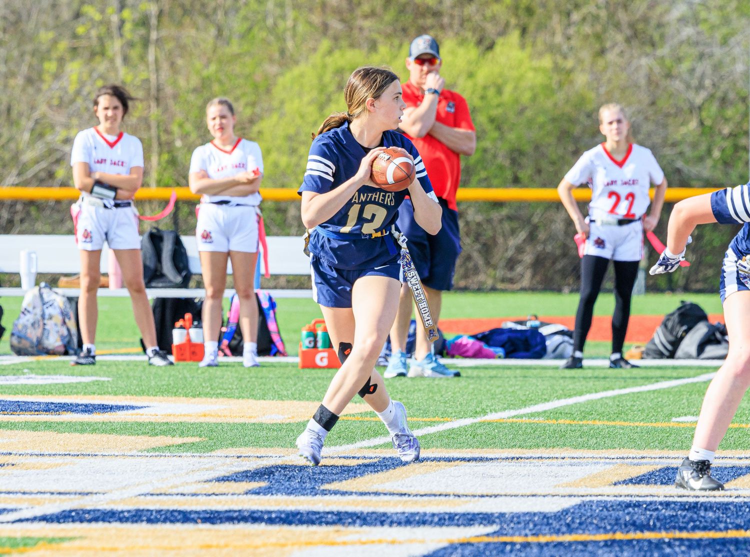 Female flag football player in navy jersey #12 prepares to throw a pass during a competitive outdoor game.