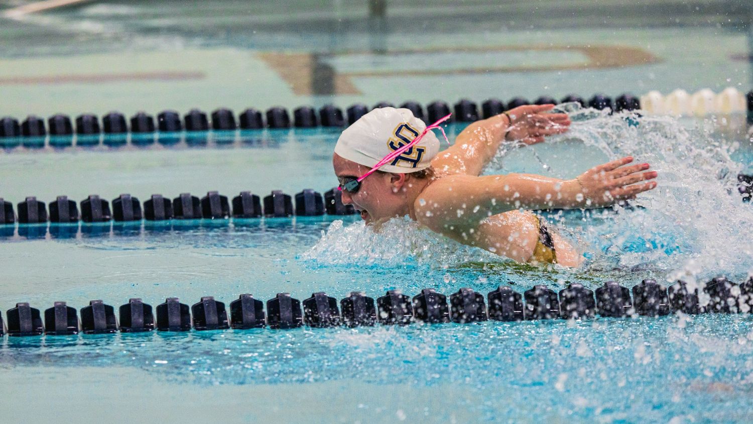 A swimmer wearing a white swim cap performs butterfly stroke during a competitive race in a pool.