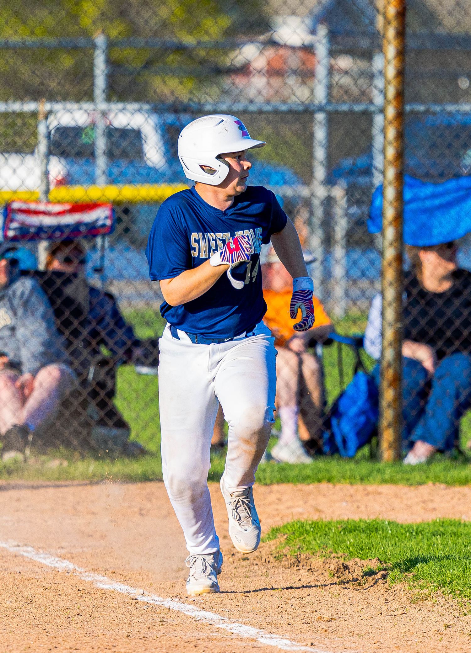 Baseball player in navy blue uniform and white helmet running down first base line during outdoor game on sunny day.