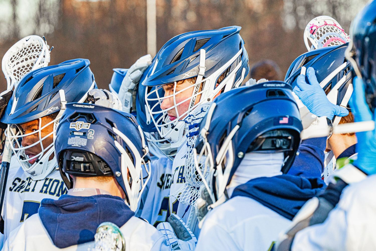 Lacrosse team huddles together in blue helmets and uniforms during an outdoor game.