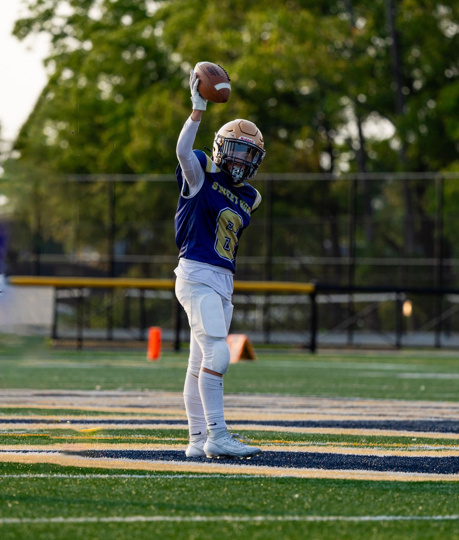 Football player in blue and gold uniform celebrating with raised arms on field.