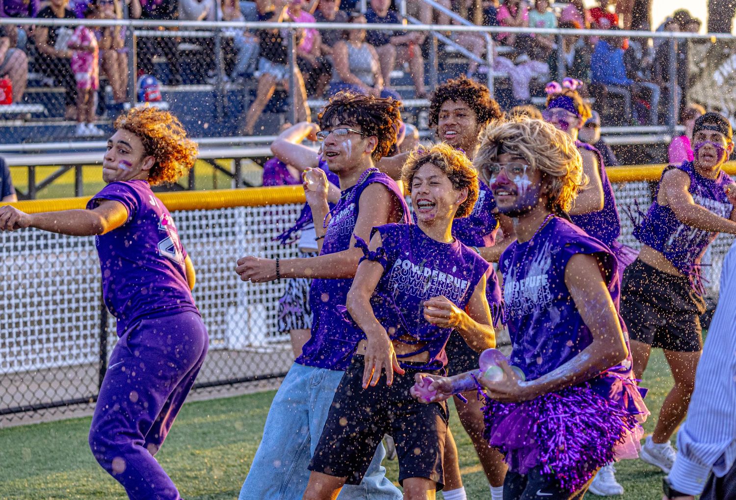 Students in purple uniforms celebrate with water spray on a football field.