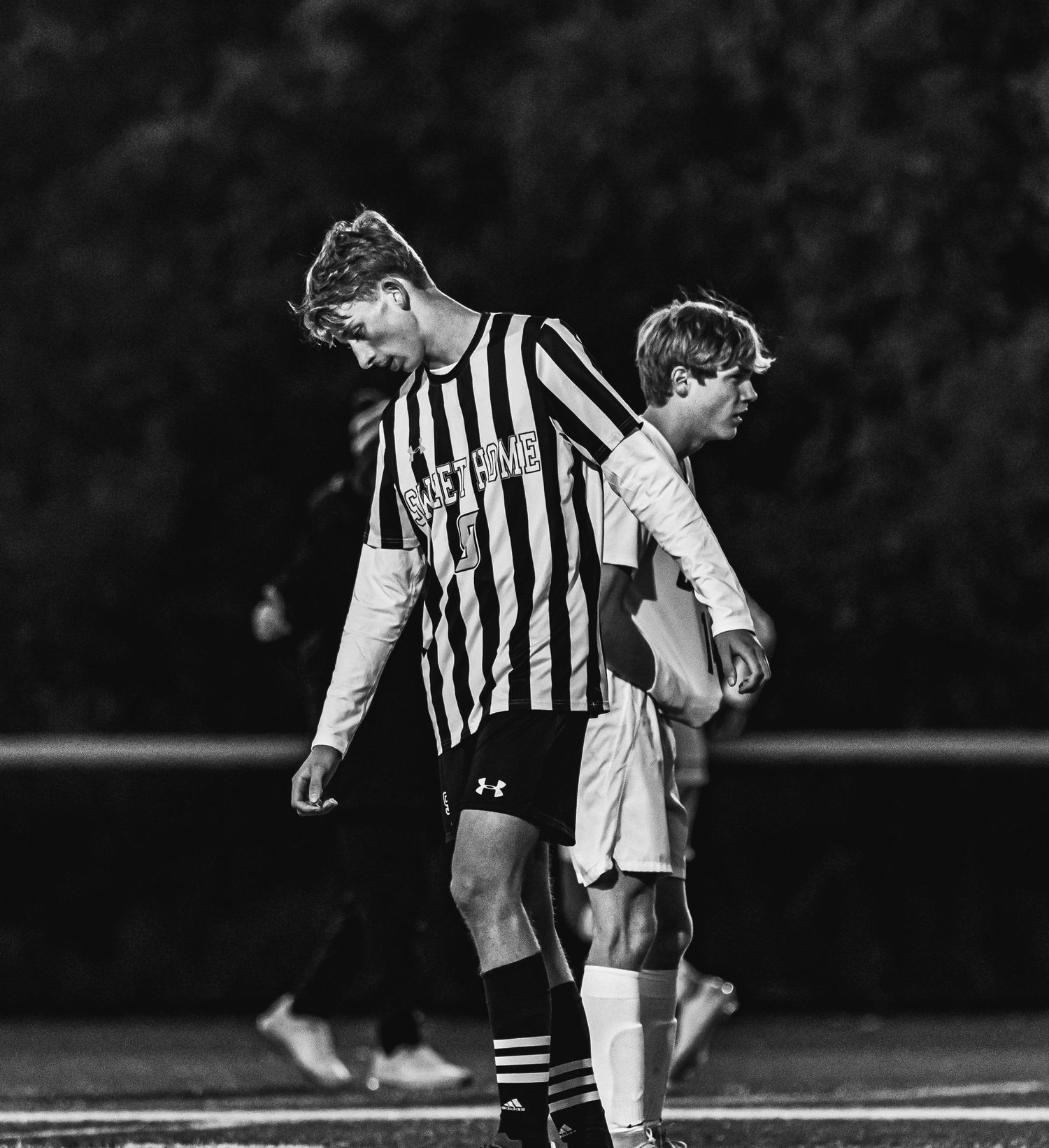 Two soccer players in black and white striped jerseys during night game.