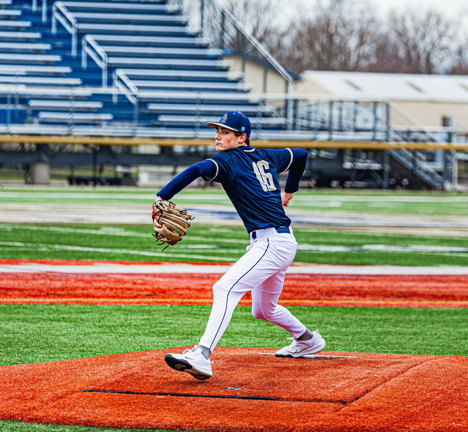 Baseball pitcher in navy uniform winding up to throw on a red turf mound during a game.