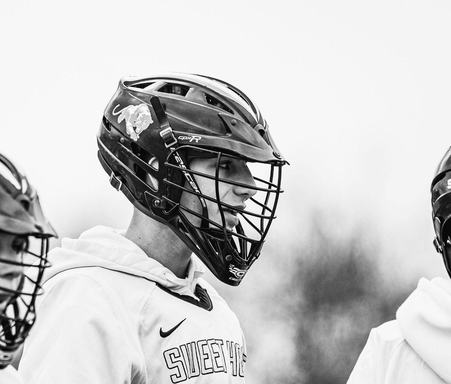Black and white photo of lacrosse players wearing helmets and Nike jerseys during a game.
