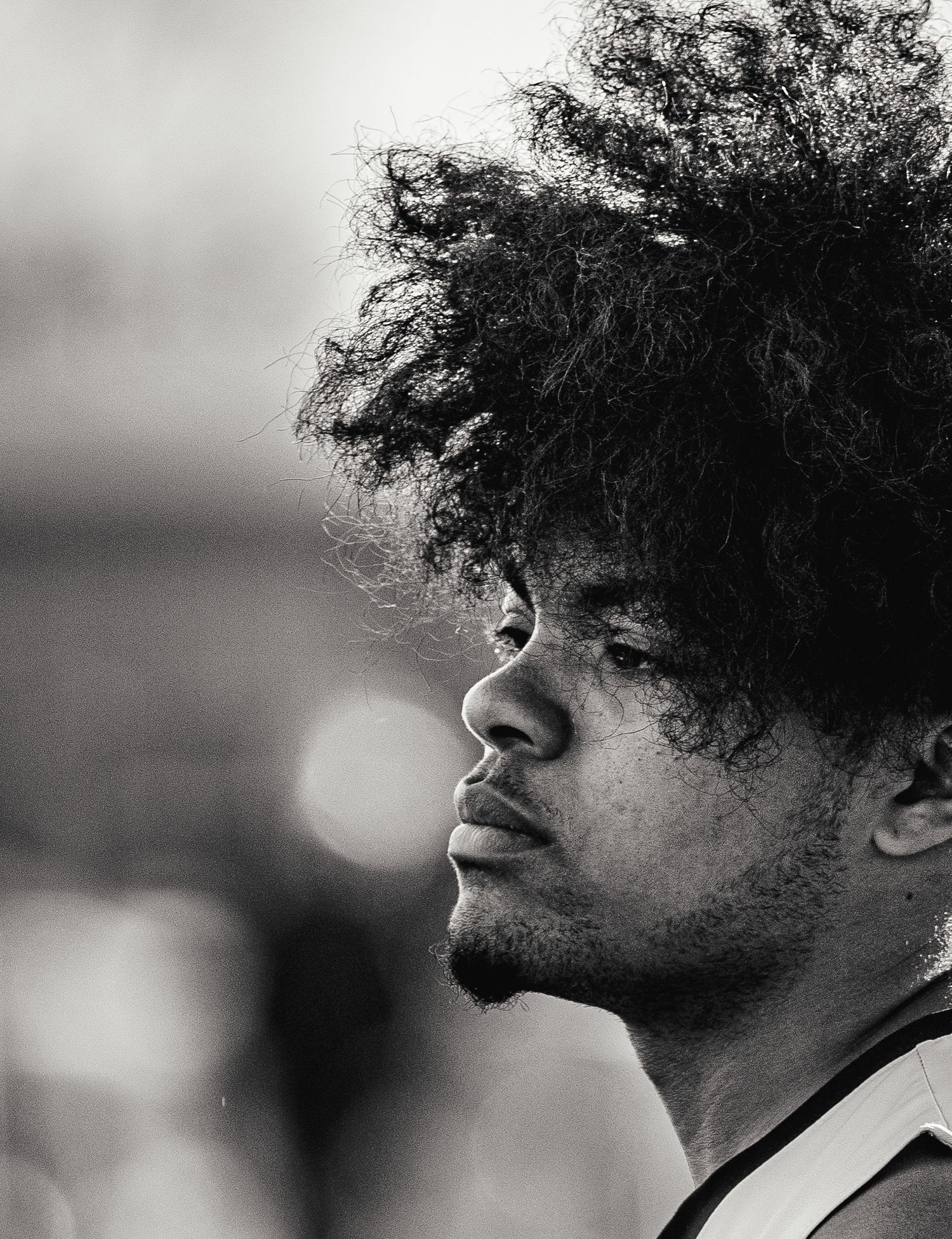 Black and white profile portrait of a young man with voluminous natural afro hair, looking contemplatively to the side.