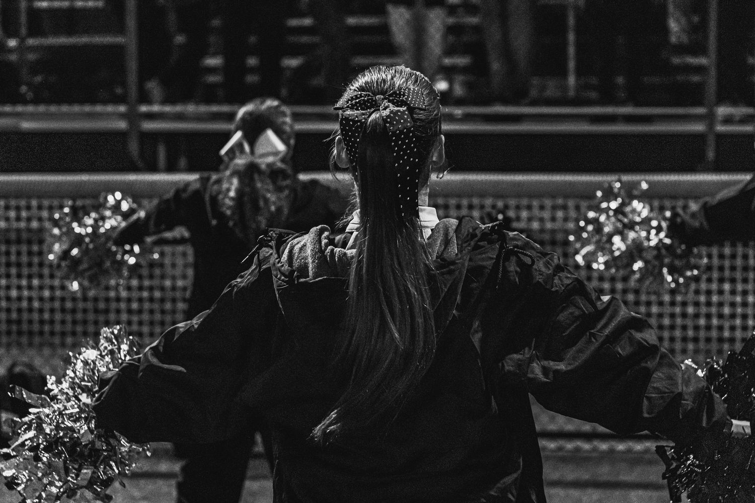 Black and white photo of a performer with long ponytail holding pom-poms at a sporting event.