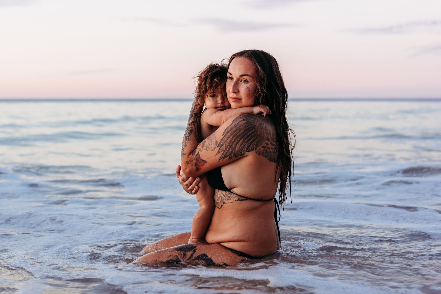 Lady sitting in the ocean embracing her baby.  Adelaide, South Australia