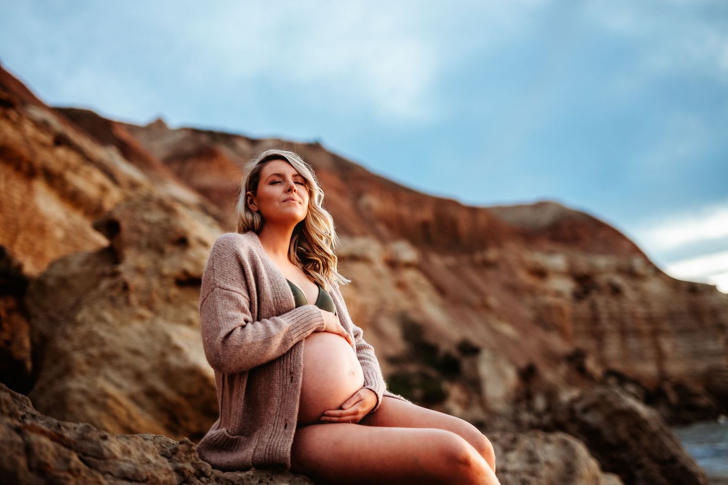 Expecting mother cradling baby bump during peaceful beach photo shoot – Raised by Water Photography