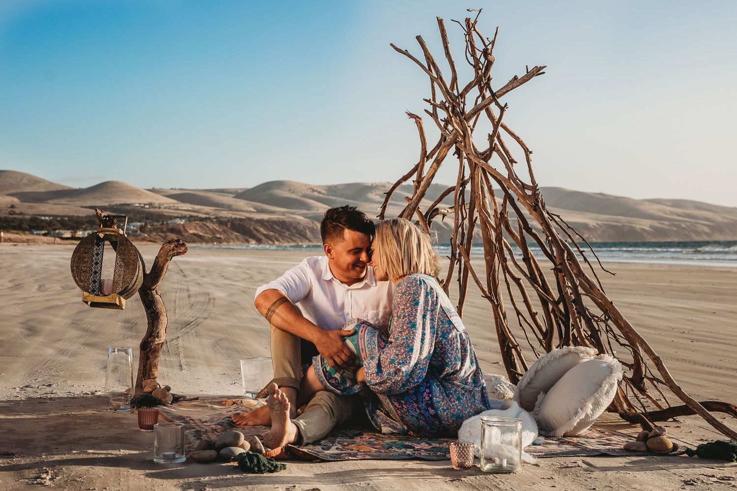 Lifestyle photo of couple by natural stick teepee on sandy beach, capturing connection and raw beauty.  Adelaide, South Australia