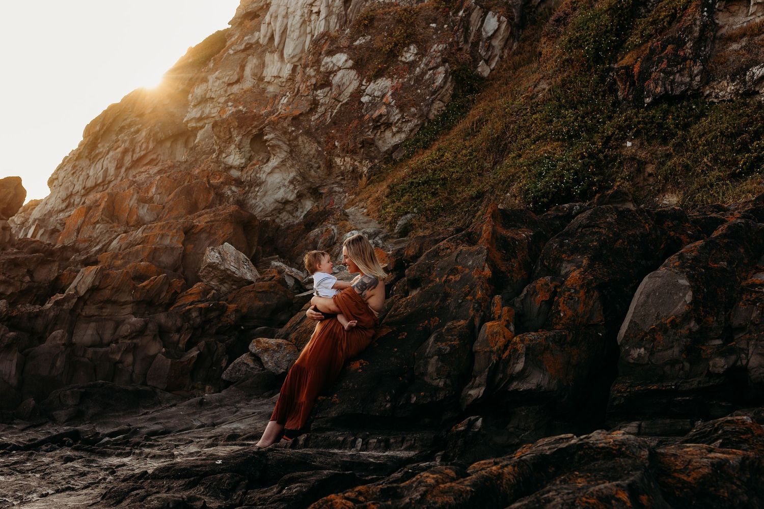Peaceful photo of mother and child sitting together on cliff overlooking the sea – South Australia family photography