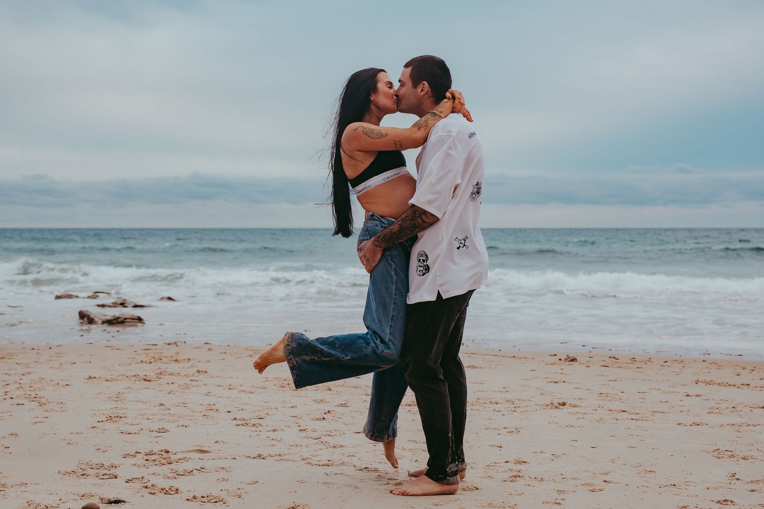 Pregnant lady with her partner kissing on the beach in Adelaide, South Australia.  Raised by Water Photography