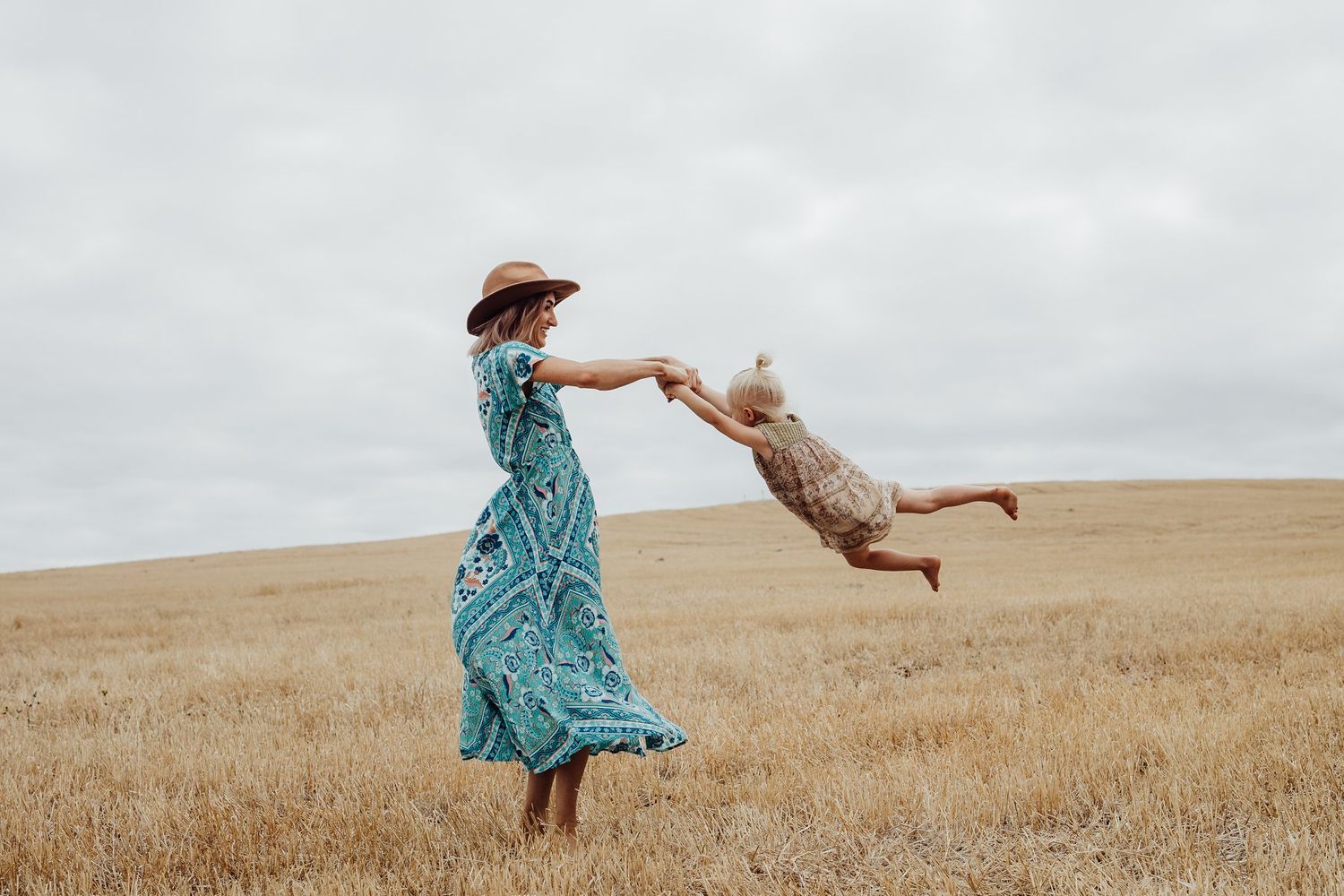 Mum spinning daughter around playfully in golden field at sunset – Raised by Water Photography, Adelaide