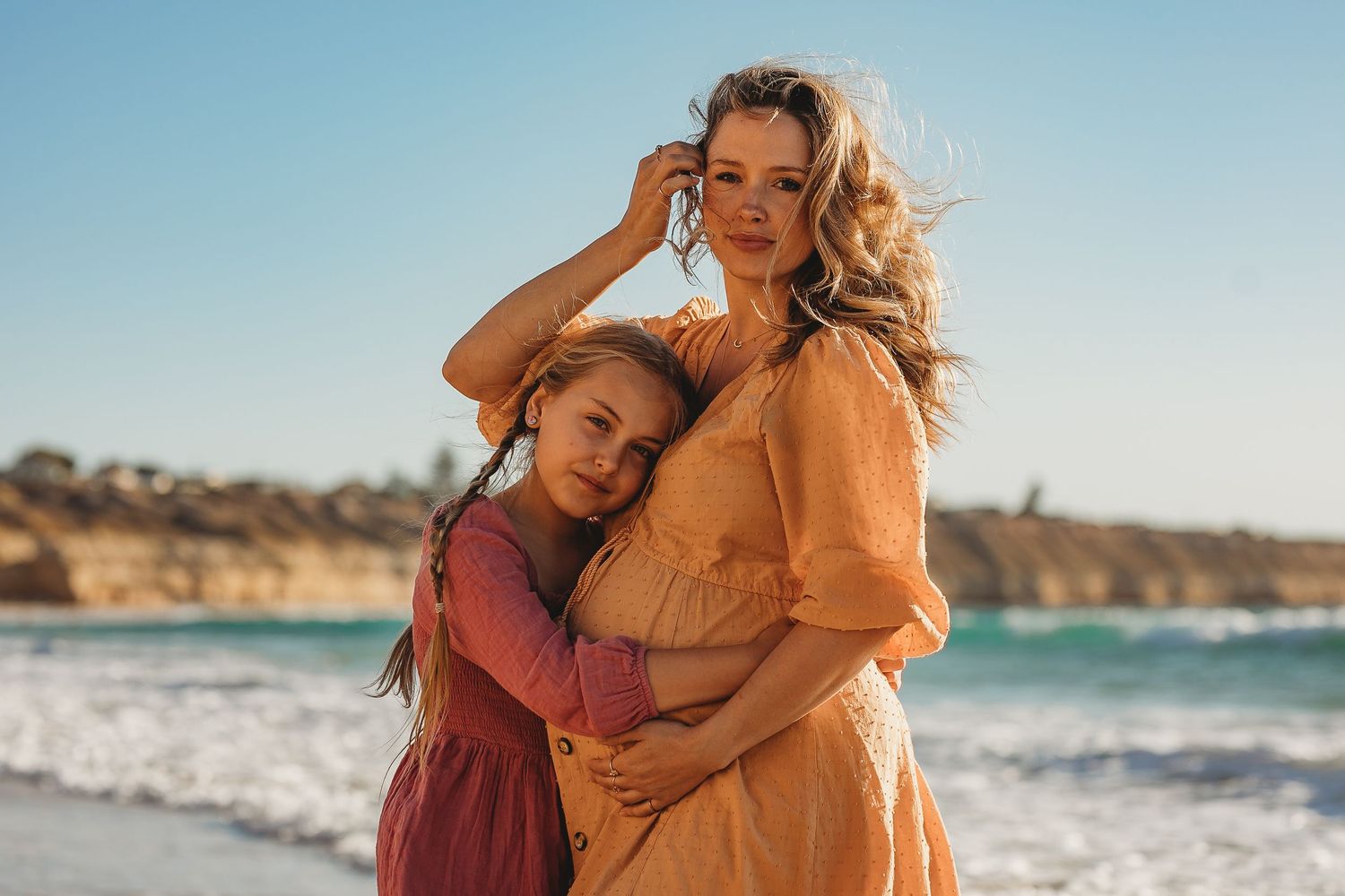 Pregnant mother and young daughter at the beach in Adelaide, South Australia, holding baby bump during sunset maternity session