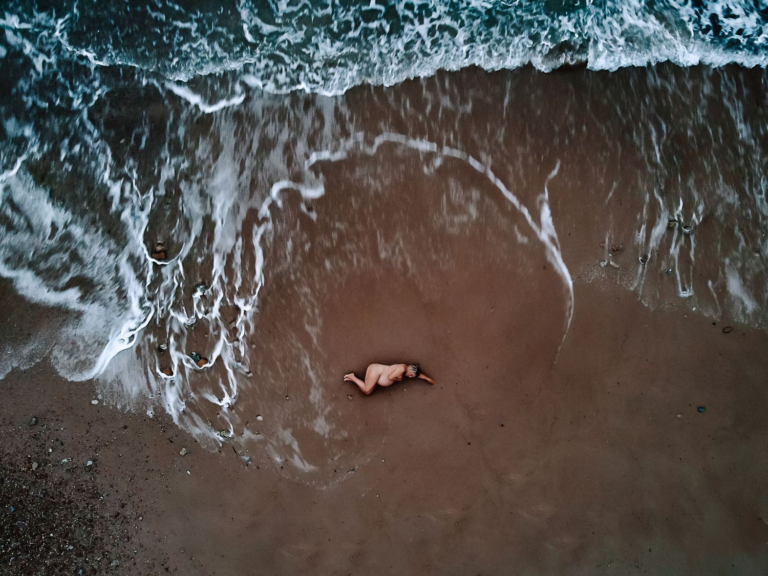 Drone photo of pregnant lady laying on the ocean embraced by a wave. Adelaide maternity drone photographer