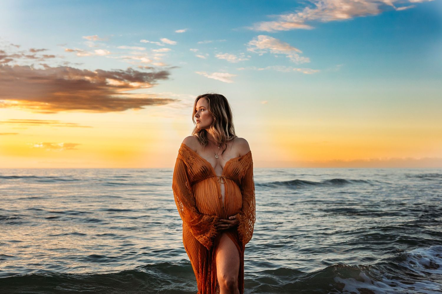 Pregnant woman standing in the ocean embracing baby bump – Raised by Water Photography