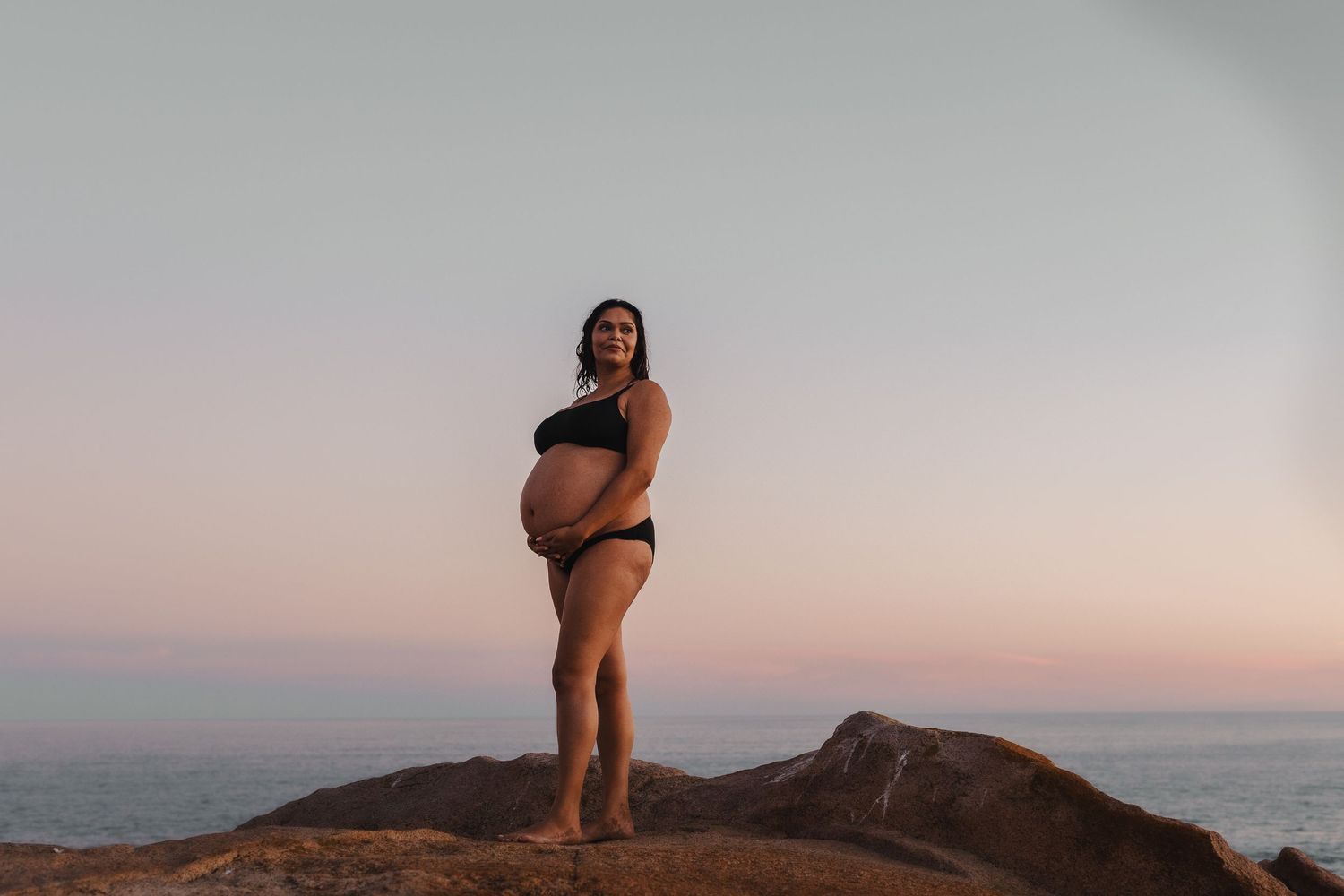 Pregnant lady standing on a cliff embracing belly.  Adelaide, South Australia